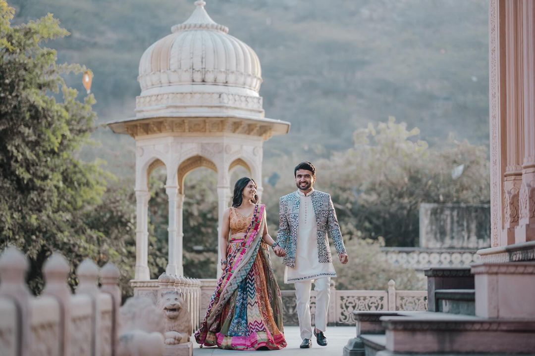 A couple in traditional attire walking at a fort, sharing bright smiles that light up the historic backdrop.